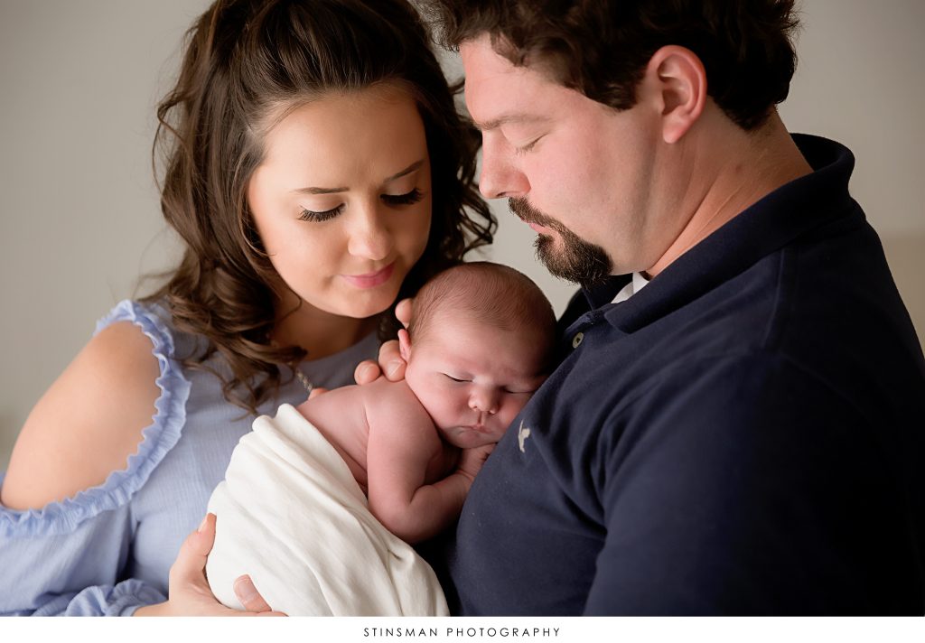 dad holding baby boy on his chest while mom snuggles in for newborn photo.
