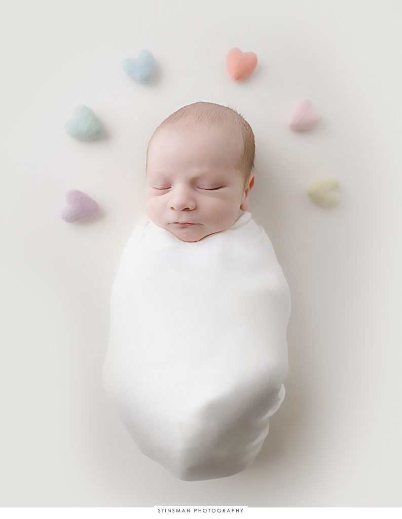 Newborn baby boy swaddled with rainbow hearts