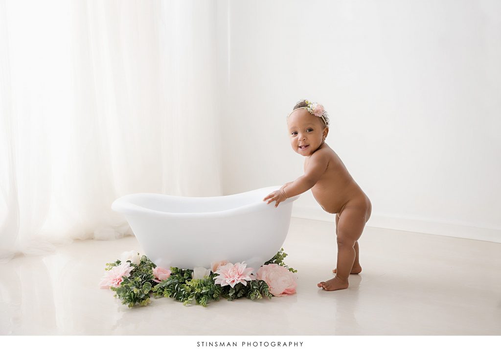 Baby girl smiling next to a tub at her 1st birthday milestone photoshoot