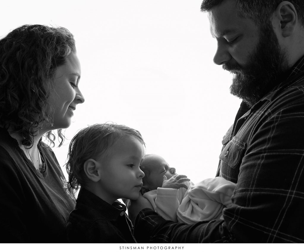 Mom, Dad, and big brother cuddling their newborn at newborn photoshoot.