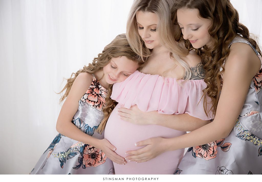 Mom and daughters snuggling her pregnant belly at her maternity photoshoot.