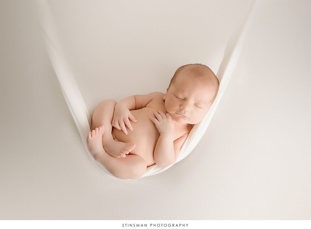 Newborn baby boy sleeping in a sling at his newborn photoshoot