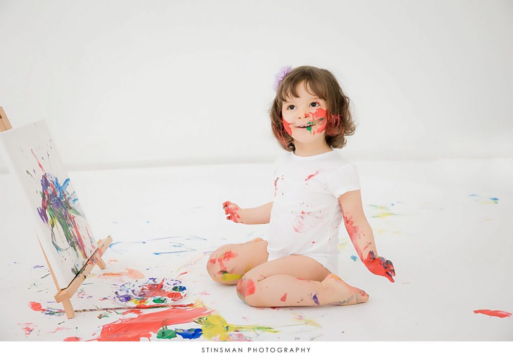 Little girl smiling and painting at her 2 year old milestone photoshoot