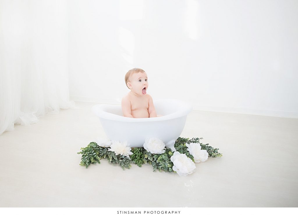 Baby girl with her tongue out during tub time at her first birthday milestone photoshoot