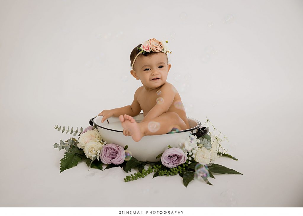 Baby girl playing in her milk bath at her first birthday milestone photoshoot