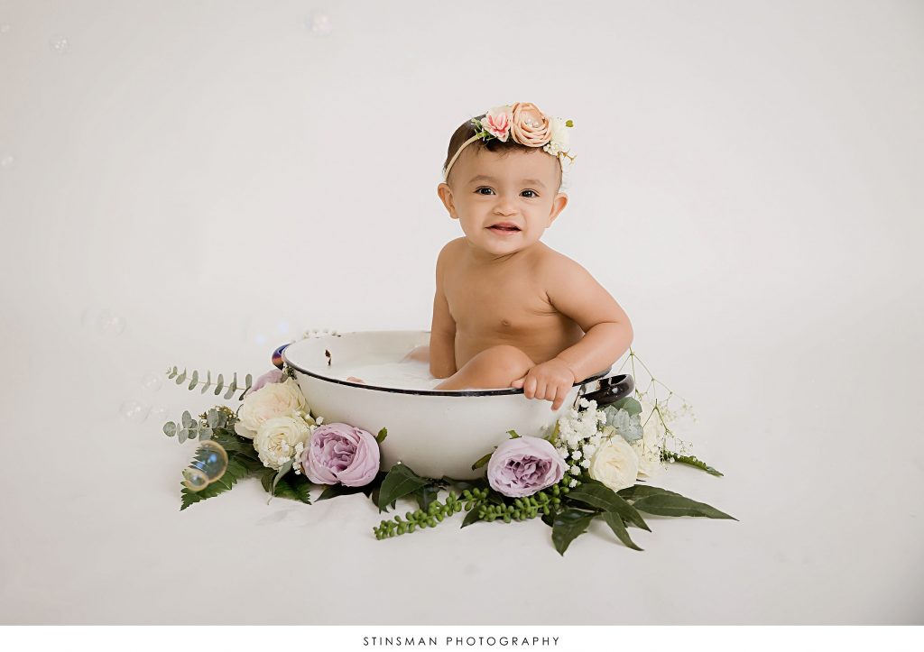Baby girl smiling in her milk bath at her first birthday milestone photoshoot
