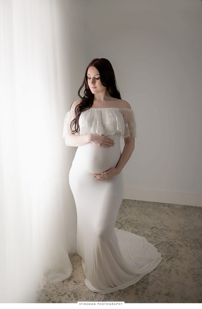 Pregnant mom posing in white dress at her maternity photoshoot