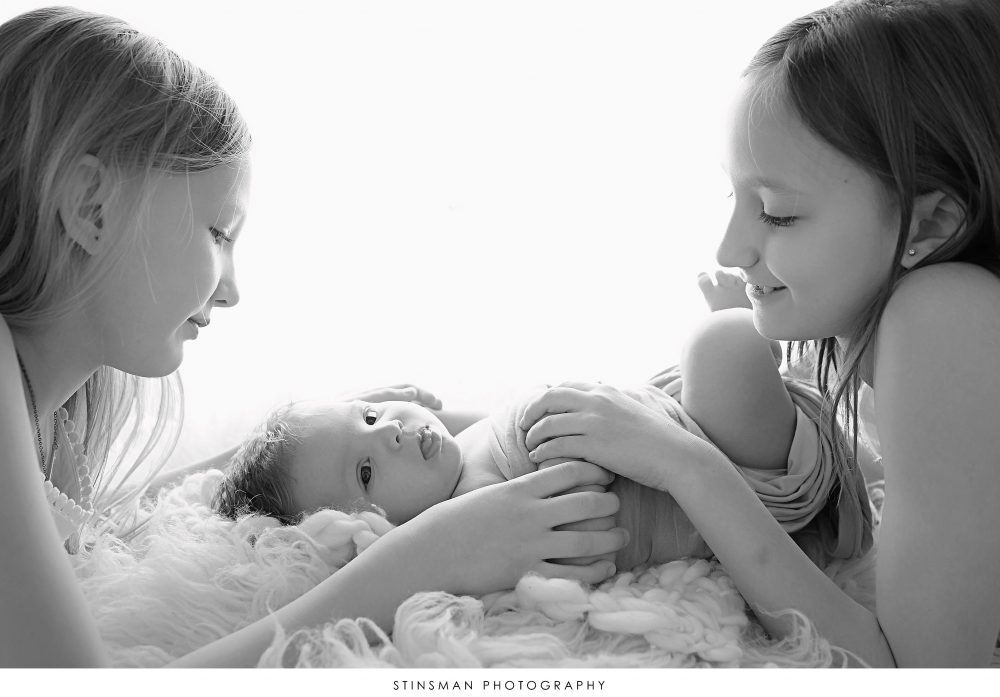 Newborn baby boy posed with his sisters at his newborn photoshoot