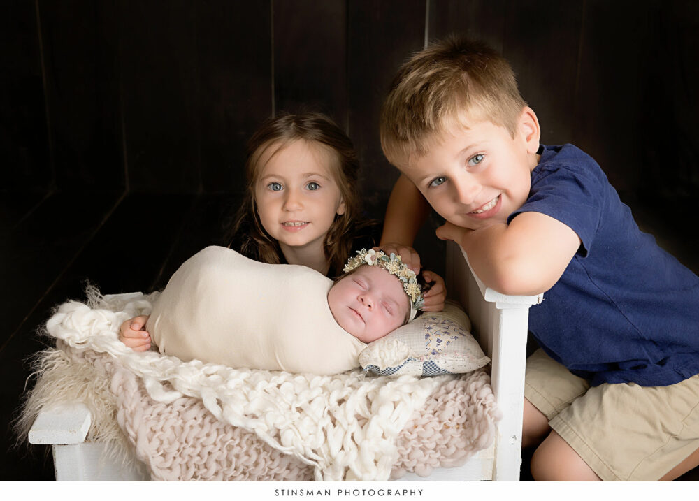 Newborn baby girl posed with her older siblings at her newborn photoshoot