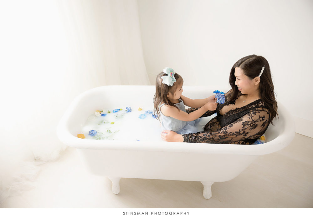 Pregnant mom playing with her daughter in a milk bath at her maternity photoshoot