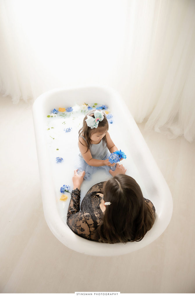 Pregnant mom playing with her daughter in milk bath at her maternity photoshoot