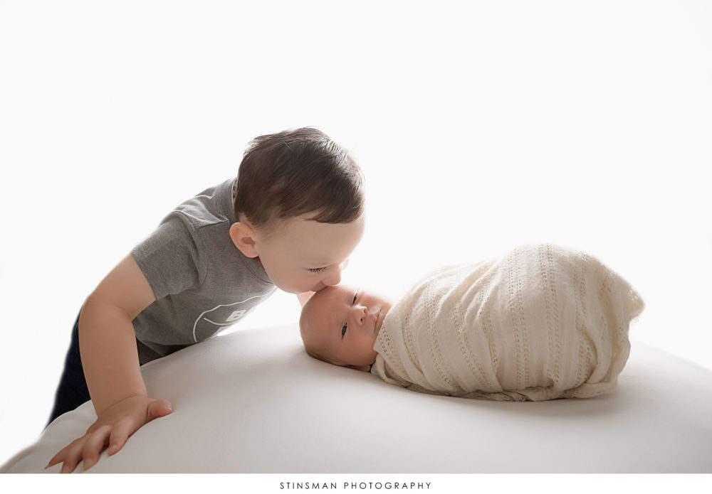 Newborn baby boy posing with his brother at his newborn photoshoot