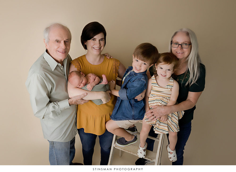 Mom, siblings, and grandparents posing with newborn baby boy at a newborn photoshoot