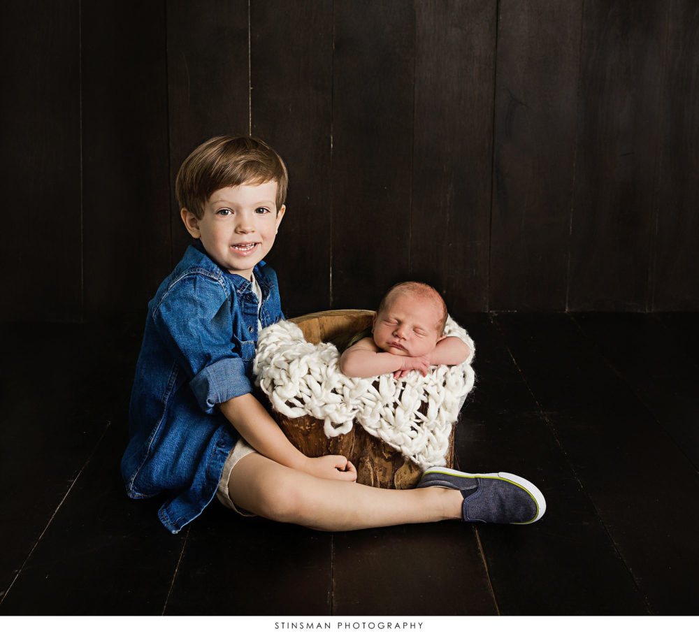 Little boy posing with his newborn brother at newborn photoshoot