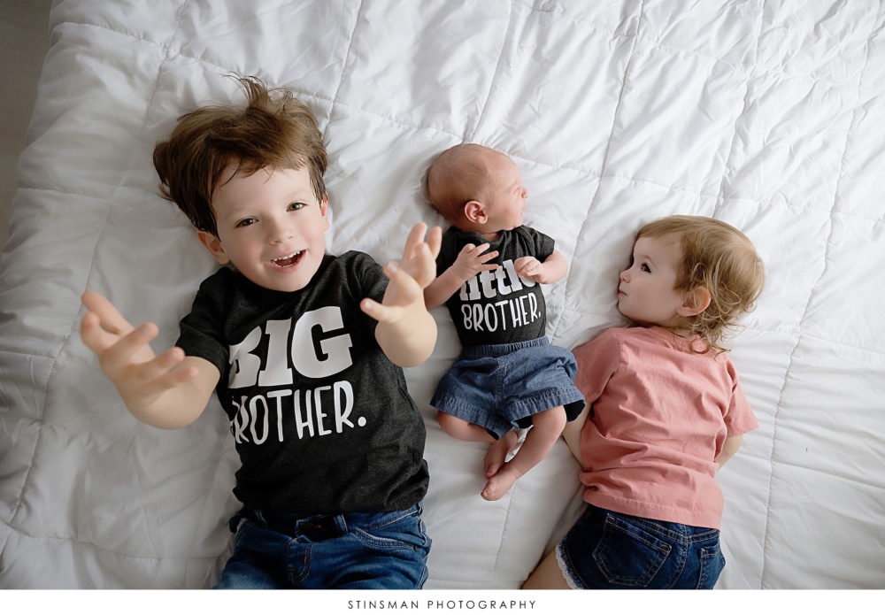 Siblings laying on a bed with their baby brother at newborn photoshoot