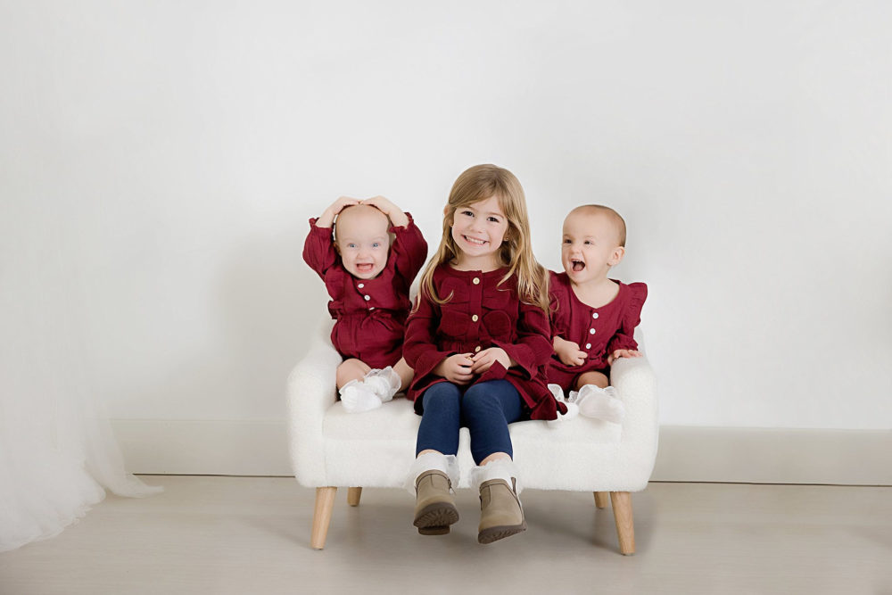 Big sister smiling with her twin sisters at their milestone photoshoot