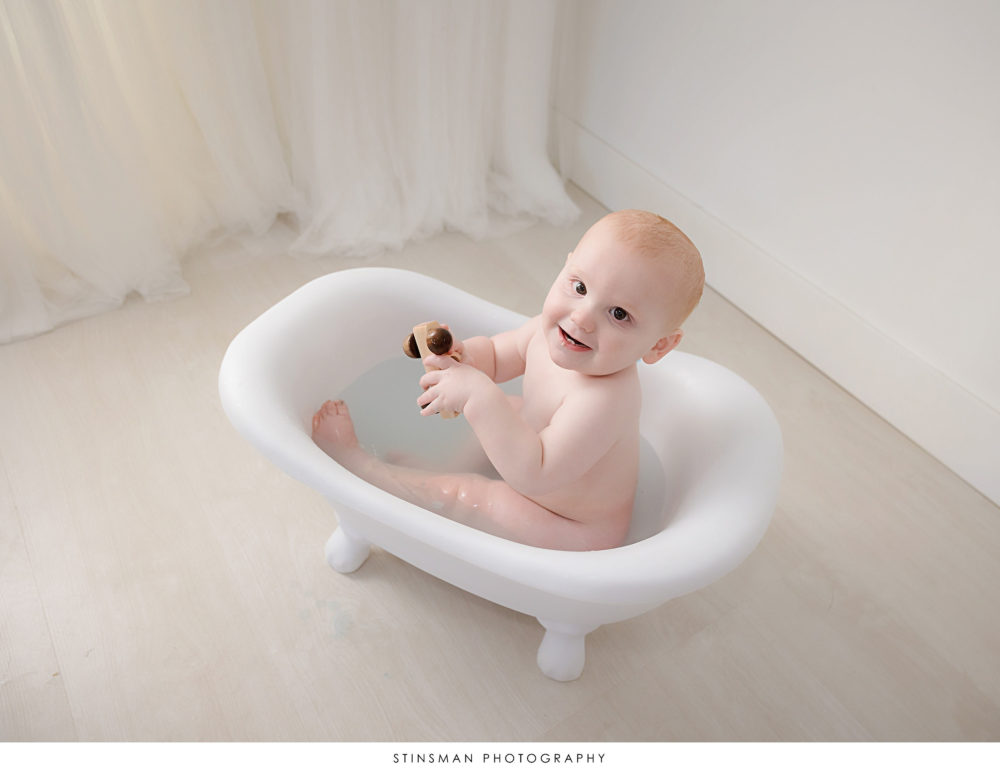 Baby boy playing in a bath at his milestone photoshoot