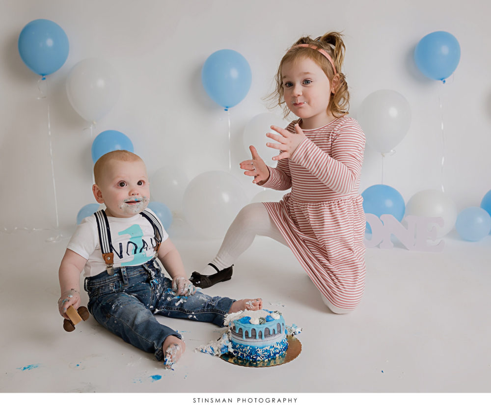 Baby boy eating his cake with sister at milestone photoshoot