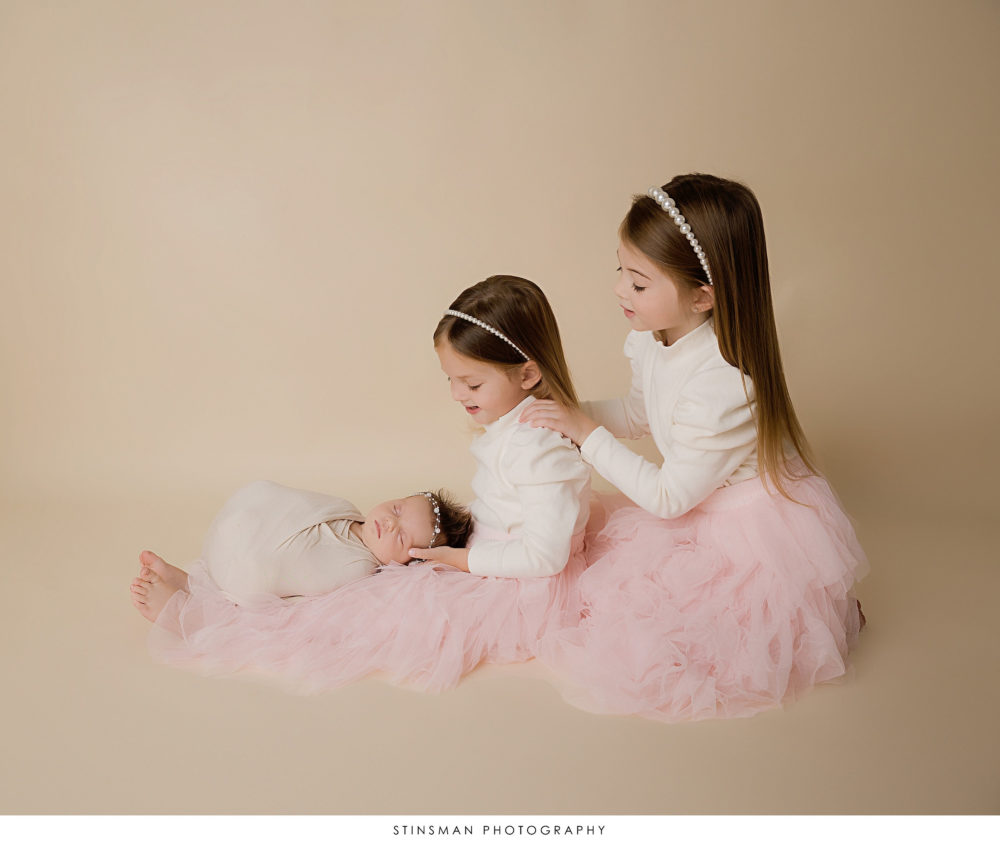 Newborn baby girl posed with her sisters at her newborn photoshoot