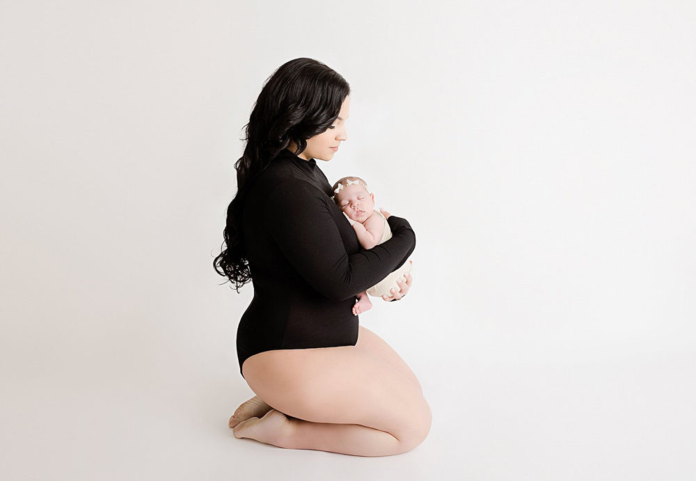 Mom posing with her newborn baby girl at their newborn photoshoot