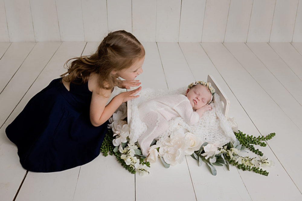 Big sister posing with her new baby sister at their newborn photoshoot