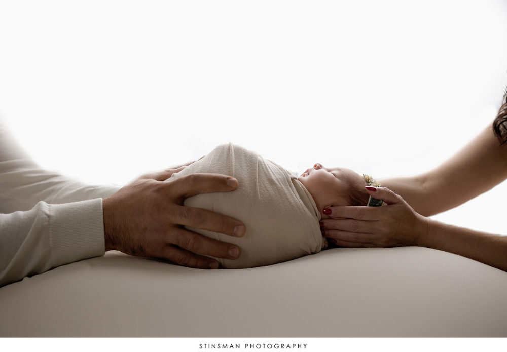 side view of newborn swaddled in wrap held by parents for in-studio photo shoot