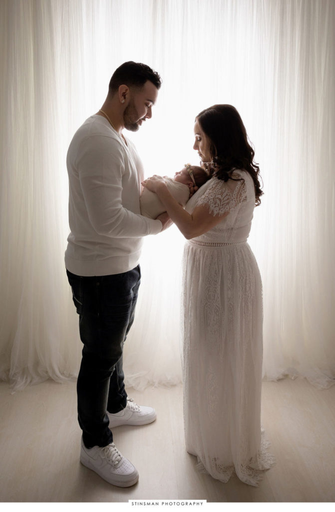 Mom and dad looking upon newborn held in each other's arms for first studio photo shoot