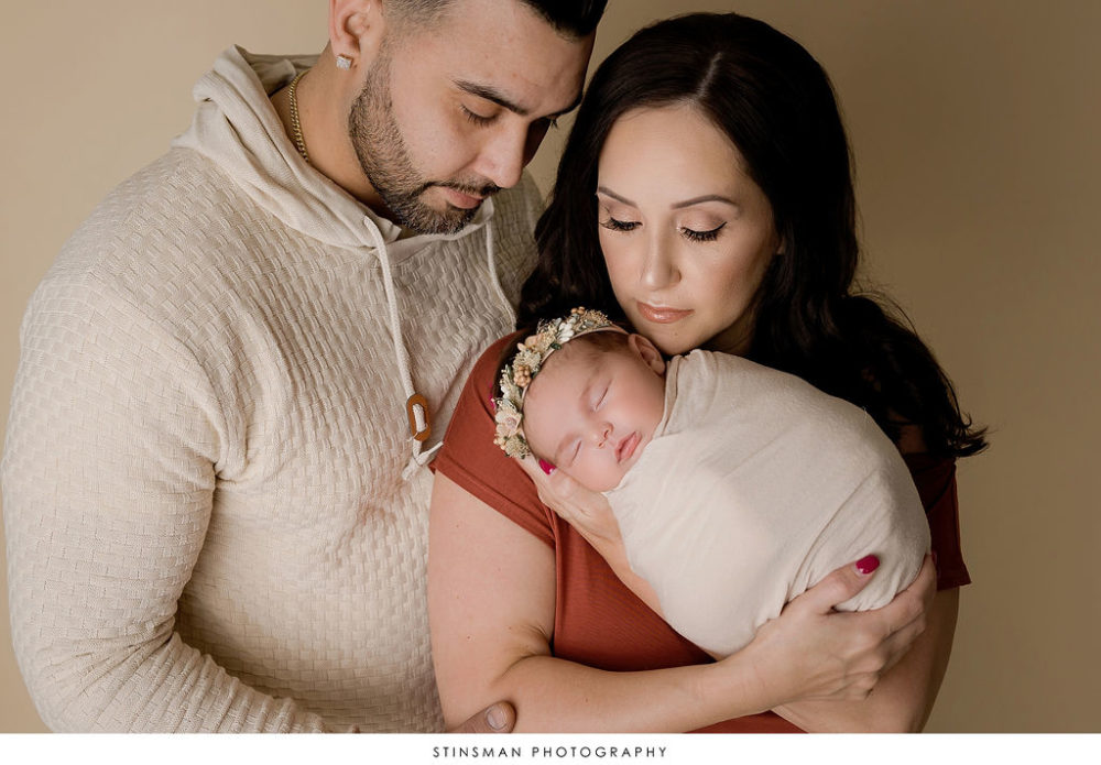 Parents looking lovingly down at new born baby girl for newborn photo shoot in new Jersey.