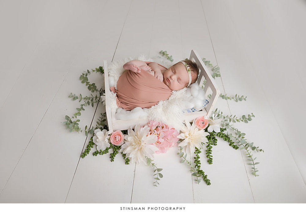 sleeping newborn baby girl wrapped in muslin with headband on crib enshrined with flowers