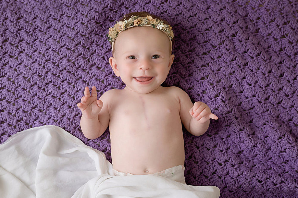 6 month baby girl with headband in with purple backdrop for newborn photoshoot in South Jersey
