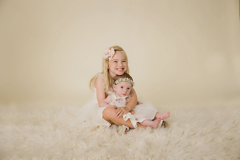 Sister and newborn baby with white and cream in-studio session for newborn portraits in Mount Laurel, New Jersey.