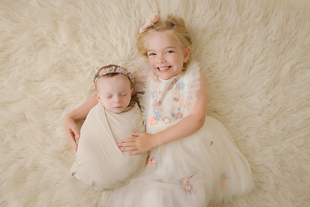 Aerial shot of young girl hugging baby sister for bright and airy in-studio newborn photography in South New Jersey.