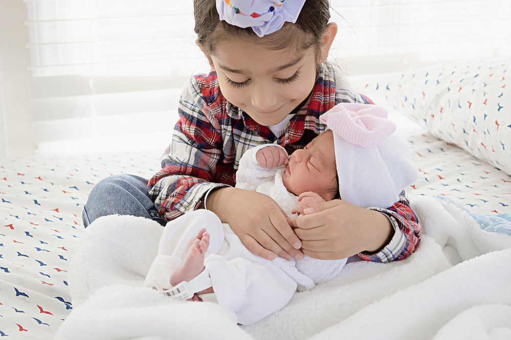 Young boy looking and holding newborn baby sister for in-home newborn session in South New Jersey.