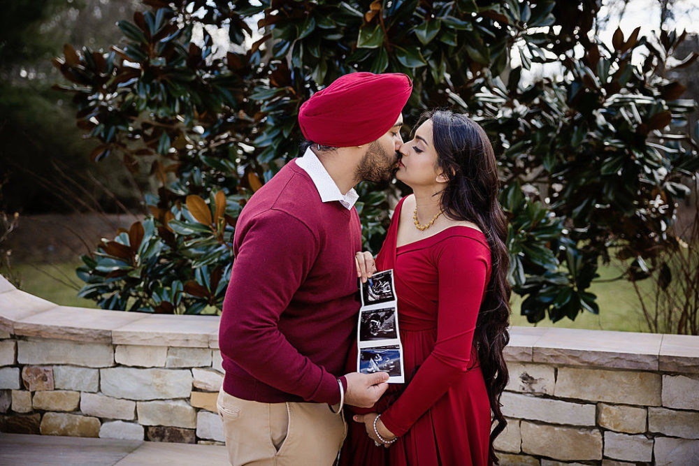 Mom and dad kiss while holding ultrasound picture of baby for pregnancy session in Voorhees, New Jersey