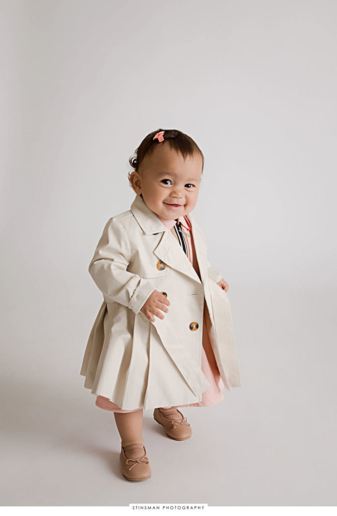 One year old girl wearing dress and trench coat for her fashionable first birthday session in Cape May, New Jersey.
