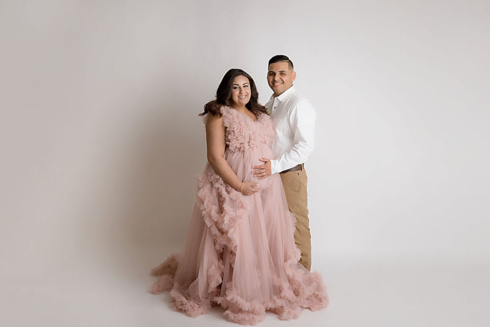 woman and man holding belly for their pop of pink in-studio maternity session in Southampton, New Jersey.