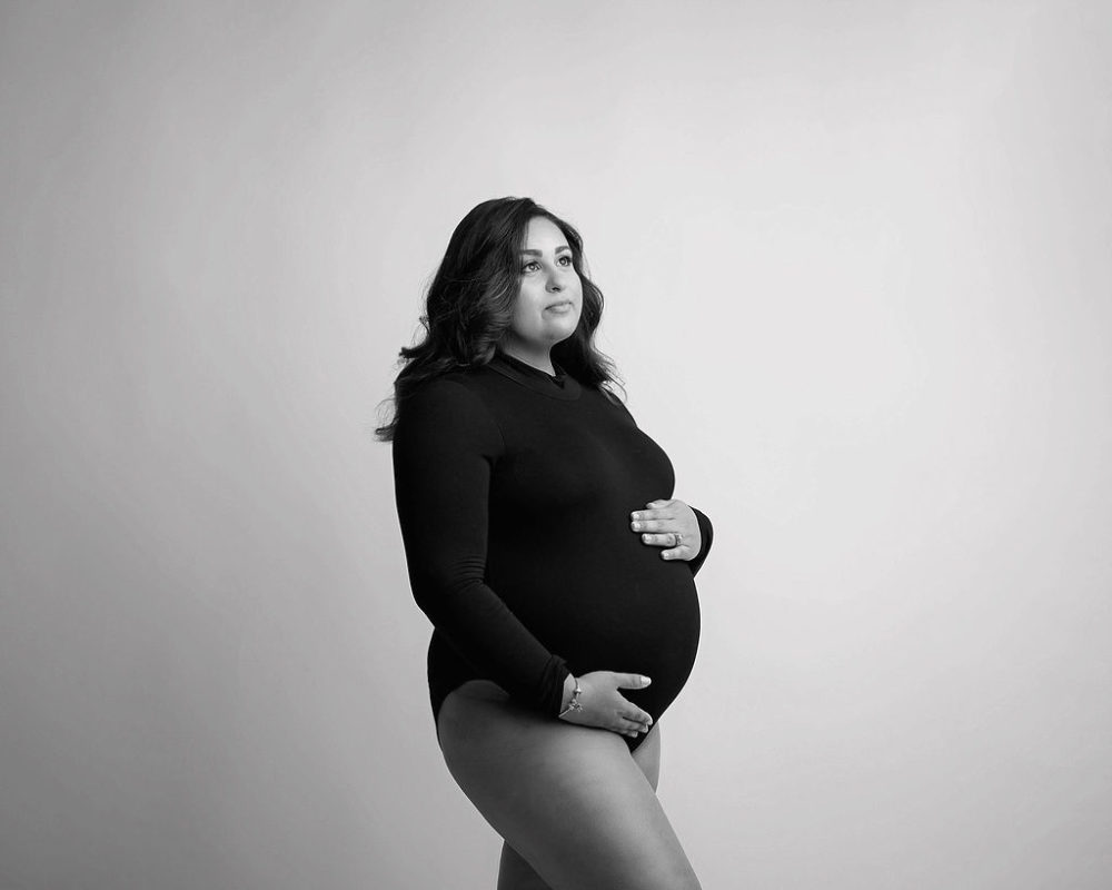 Mom wearing bodysuit holding her belly for her in-studio professional maternity photos in Pemberton, New Jersey.