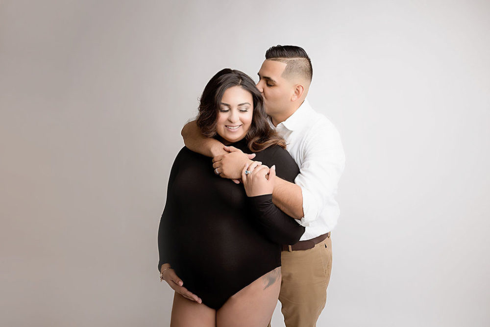 Husband kissing wife for her pop of pink in-session maternity session in South Jersey.