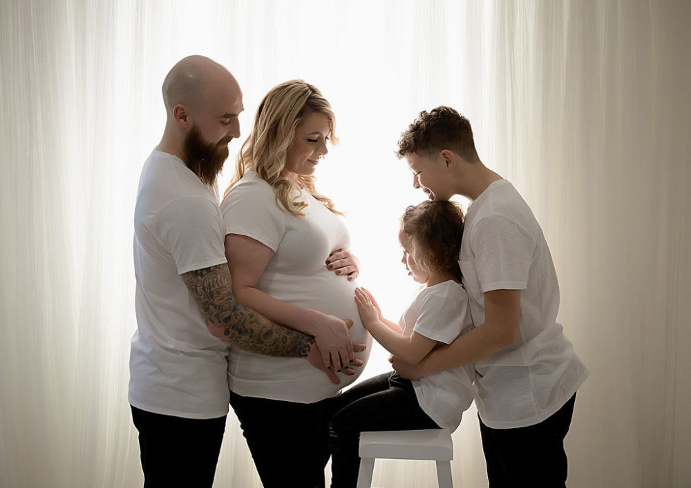 Family of four holding moms belly for her black-and-white maternity and newborn session in Hamilton, New Jersey.