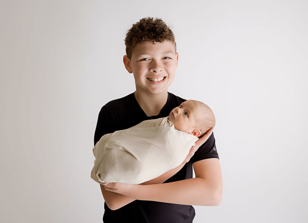 Big brother holding newborn sibling for professional baby pictures in Elizabeth, New Jersey.