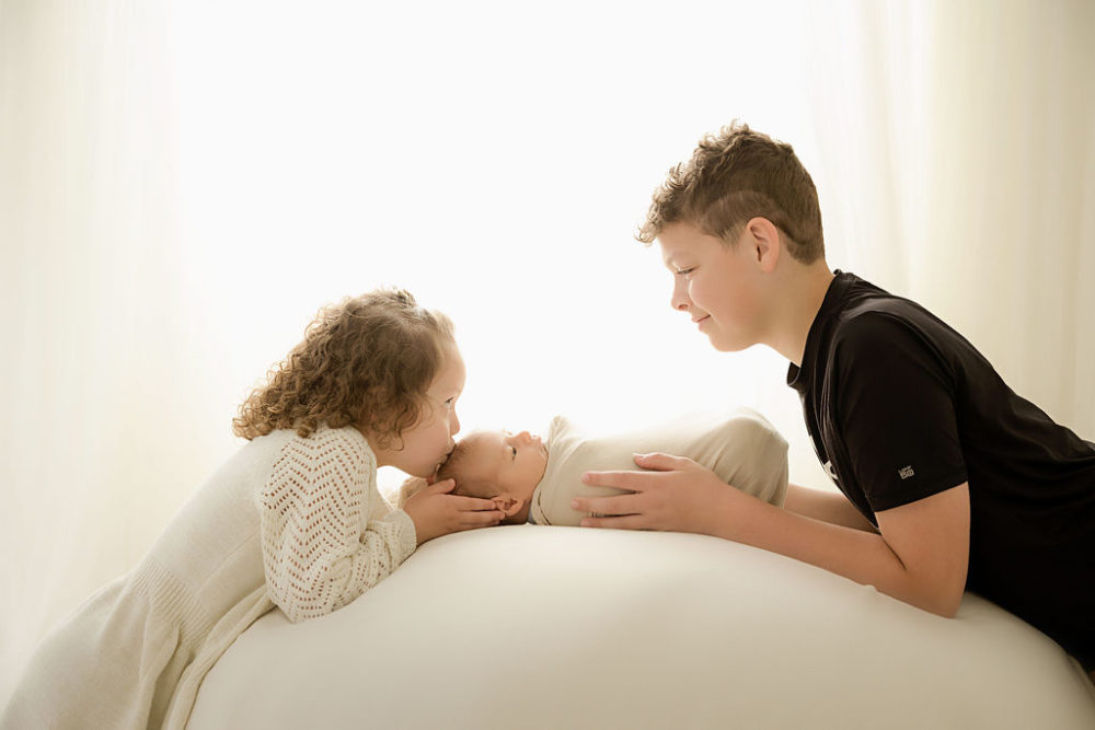 young boy and sister holding their newborn brother for a newborn portrait in Jackson, New Jersey.