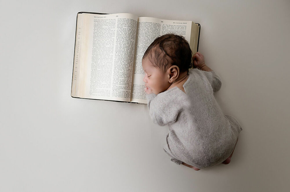 Newborn boy wearing onesie sleeping on family bible for his warm and earthy newborn session in Princeton, New Jersey.