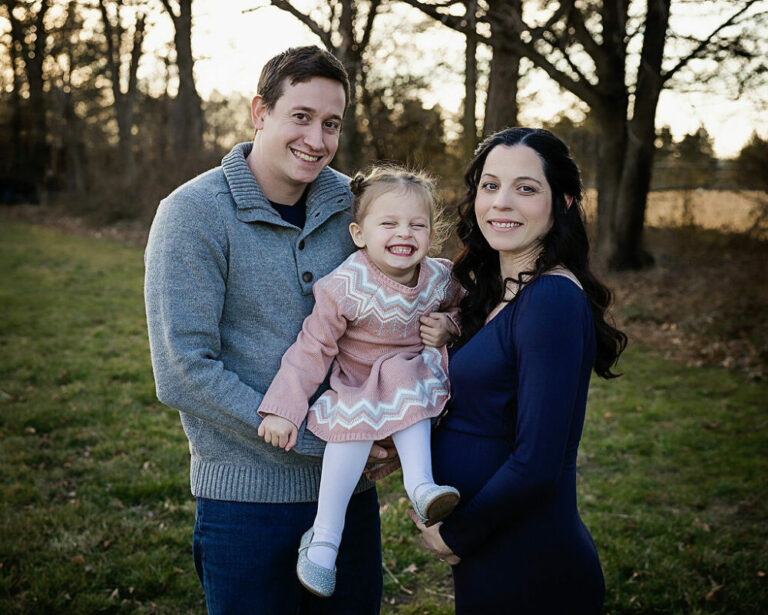 Mom, Dad and child smiling at camera for her navy blue maternity session in Trenton, New Jersey.