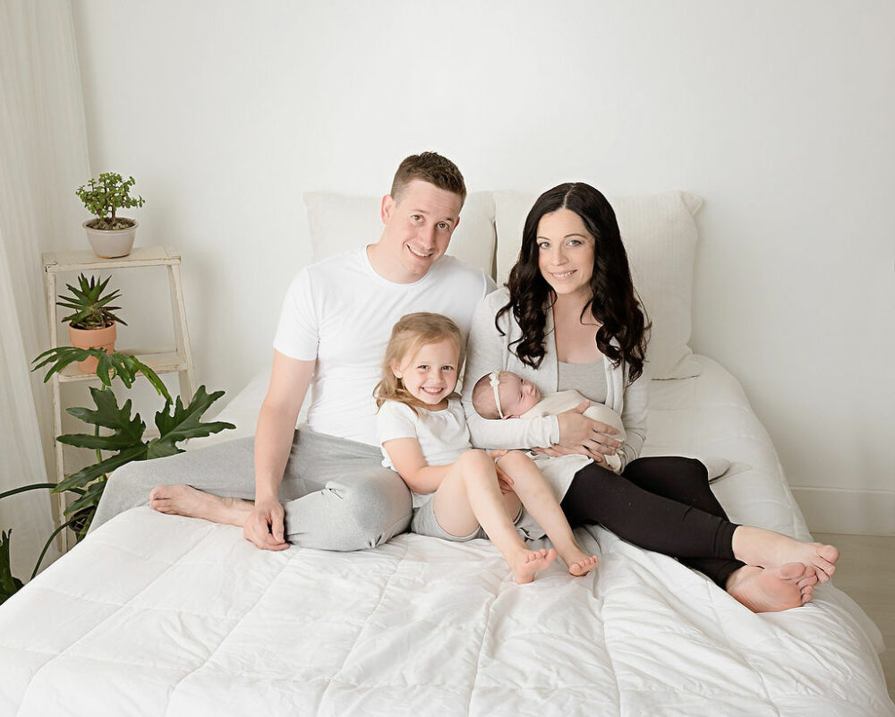 Mom called a newborn baby with her husband and first daughter on bed for her newborn baby photography session in Hoboken, New Jersey