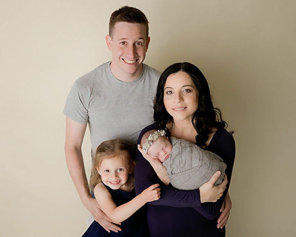 Smiling mom and dad with two daughters for a navy blue maternity and newborn session in Waterford, New Jersey