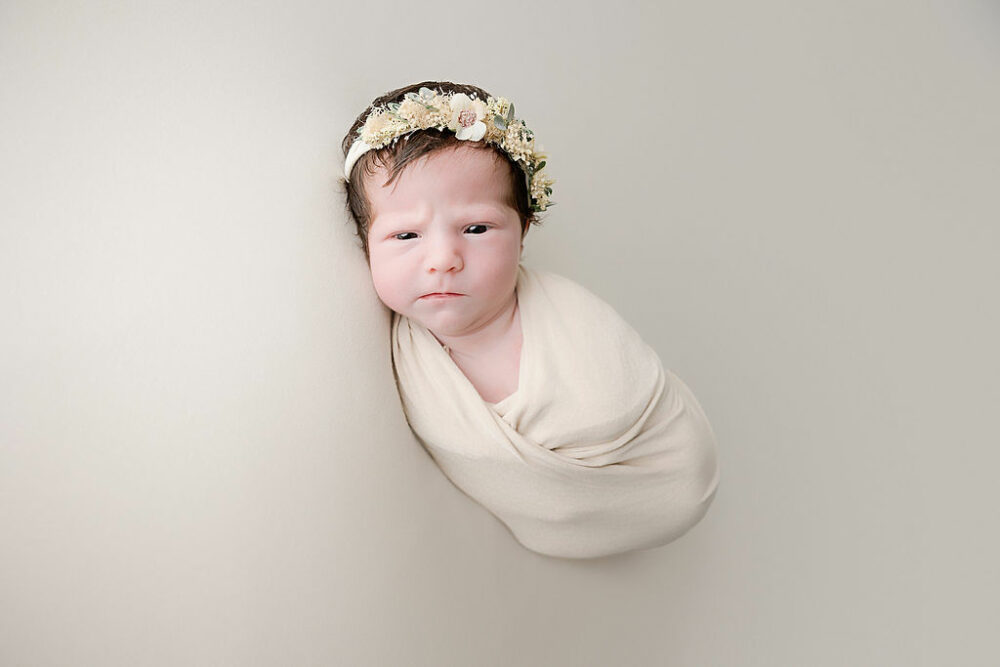 newborn girl looking at camera in swaddle and headband for her in studio newborn session in Bordentown, New Jersey.
