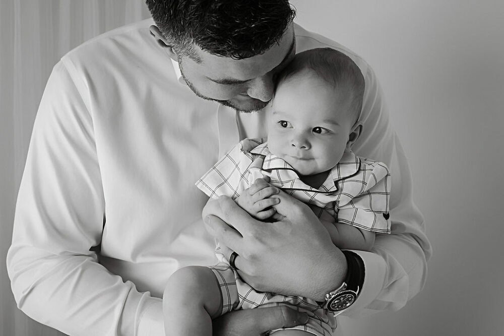 Father holding son in his arms is it in the house for an in-studio black-and-white photography session in Cinnaminson, New Jersey