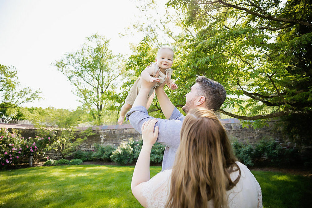 Lifestyle image of mom and dad holding baby in the air for their summer fun family session in Morristown, New Jersey.