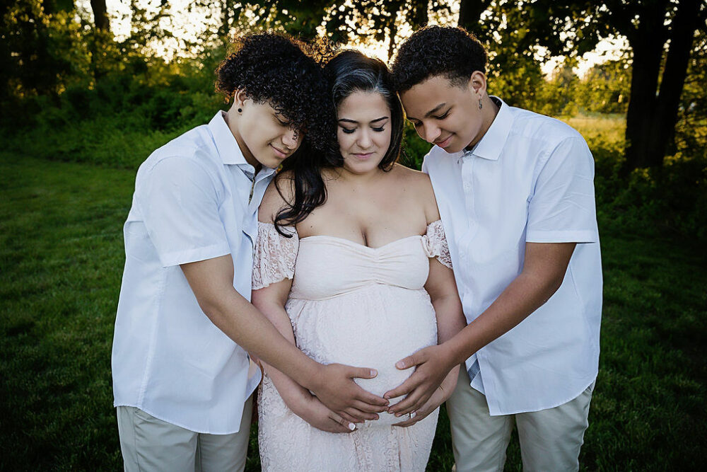 Pregnant mom with her two sons holding her belly outside for her light and radiant maternity session in Southampton, New Jersey.