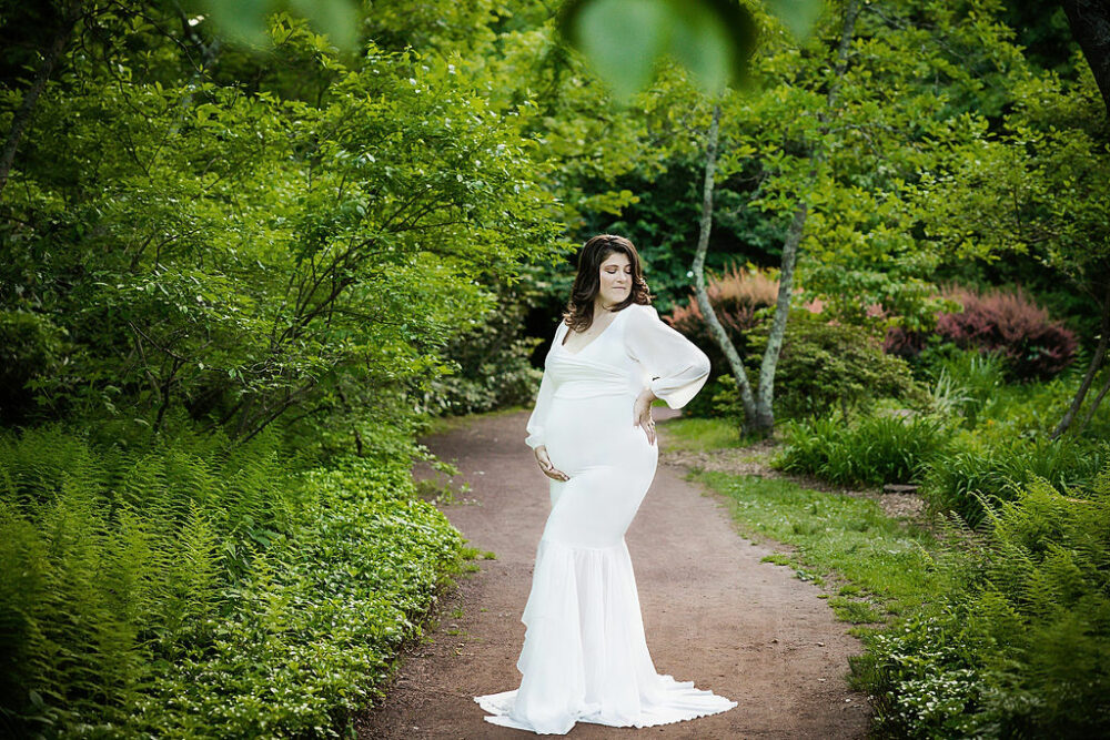 Pregnant woman holding belly and doing maternity photoshoot poses for her summer garden maternity session in Cherry Hill, New Jersey.